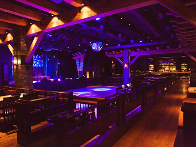 Inside the Ranch Saloon showing a wooden dance floor, stage, guitar disco ball, tables and chairs, and a bar.