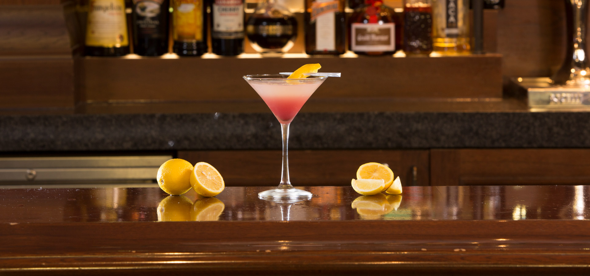 Pink liquor in a cocktail glass with a slice of lemon placed on a table