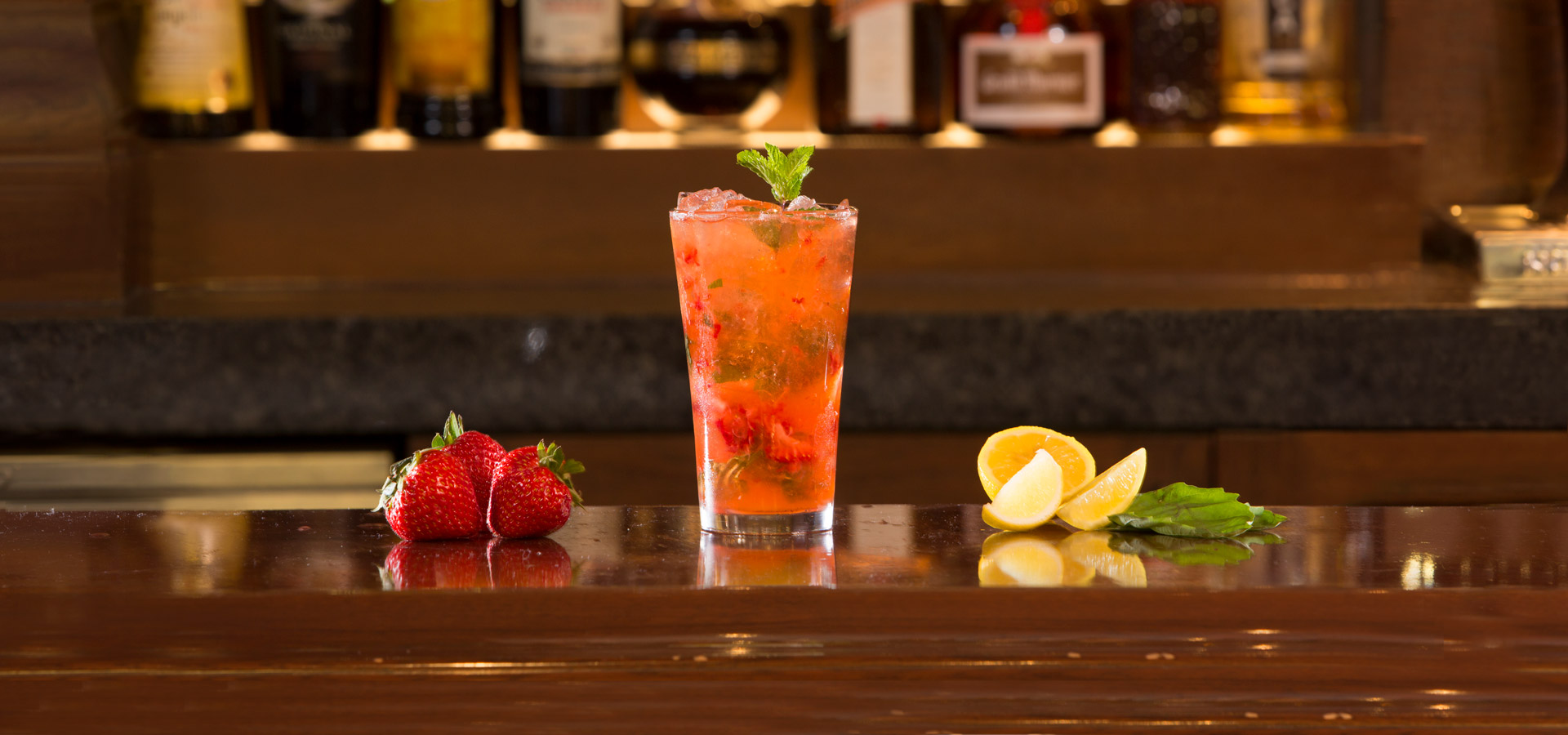 Pink liquor with sliced strawberries and mint in a glass placed on a table with various fruits