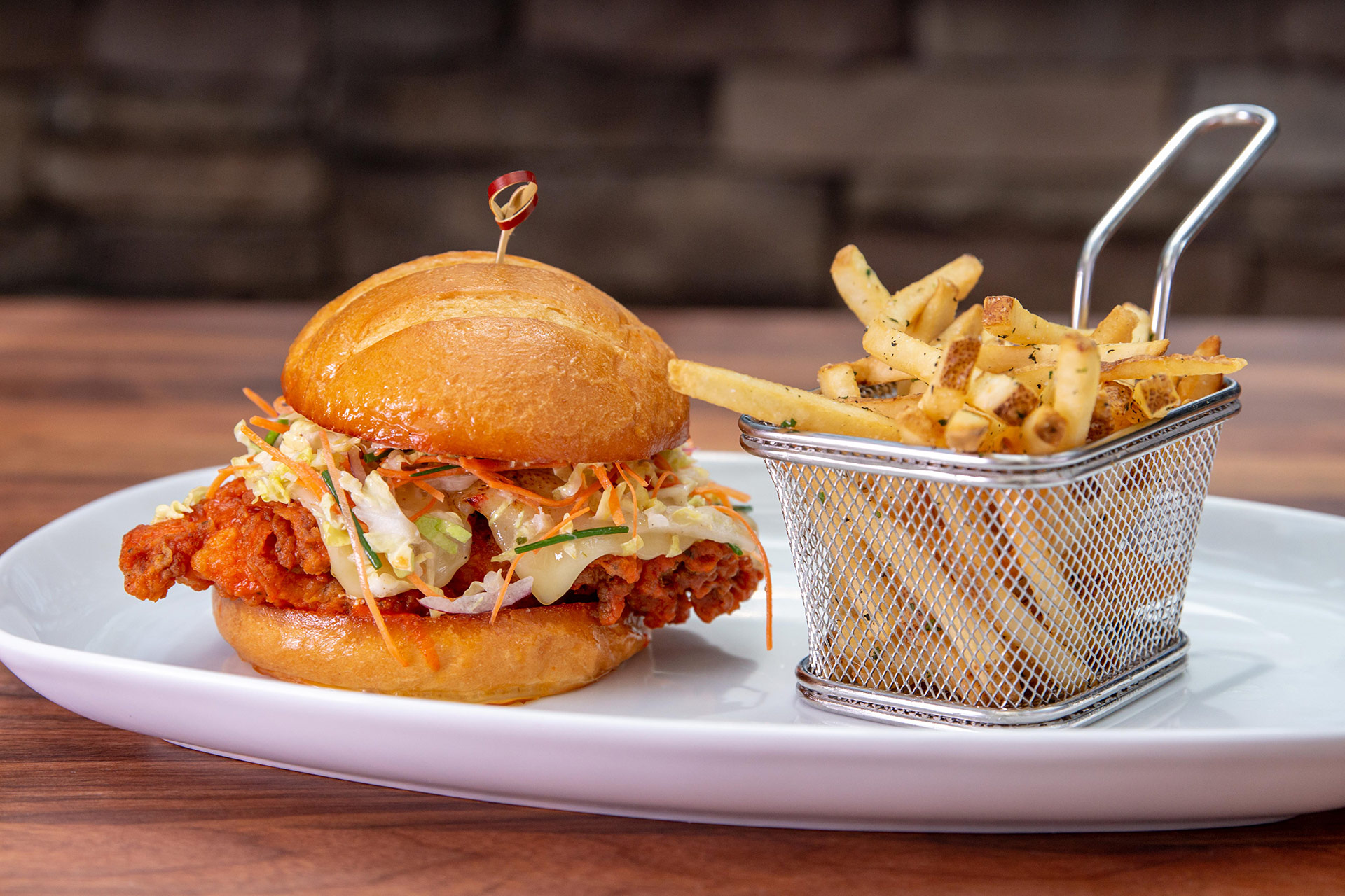 A breaded chicken burger with coleslaws and cheese placed next to a basket of french fries