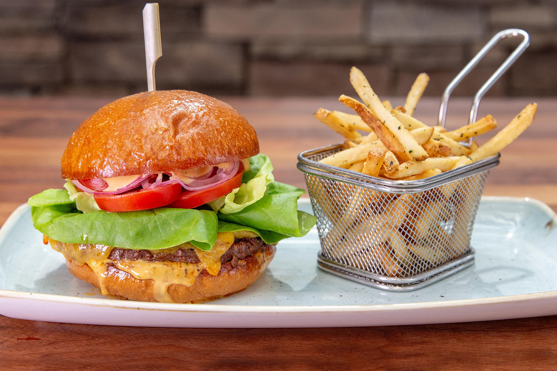 A steak burger with cheese, lettuce, and tomatoes placed next to a basket of french fries