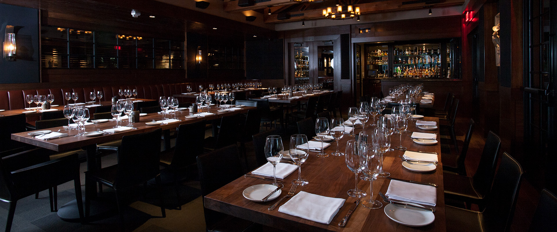 A wood-paneled room with long dining tables, chairs, and a bar