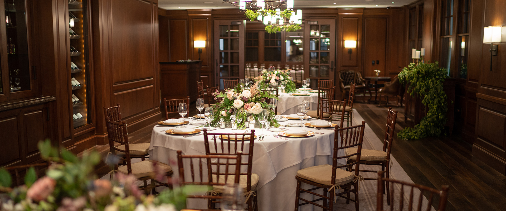 A room with wood floor, ceiling, panels, round tables, built-in wine cabinets, and a bar