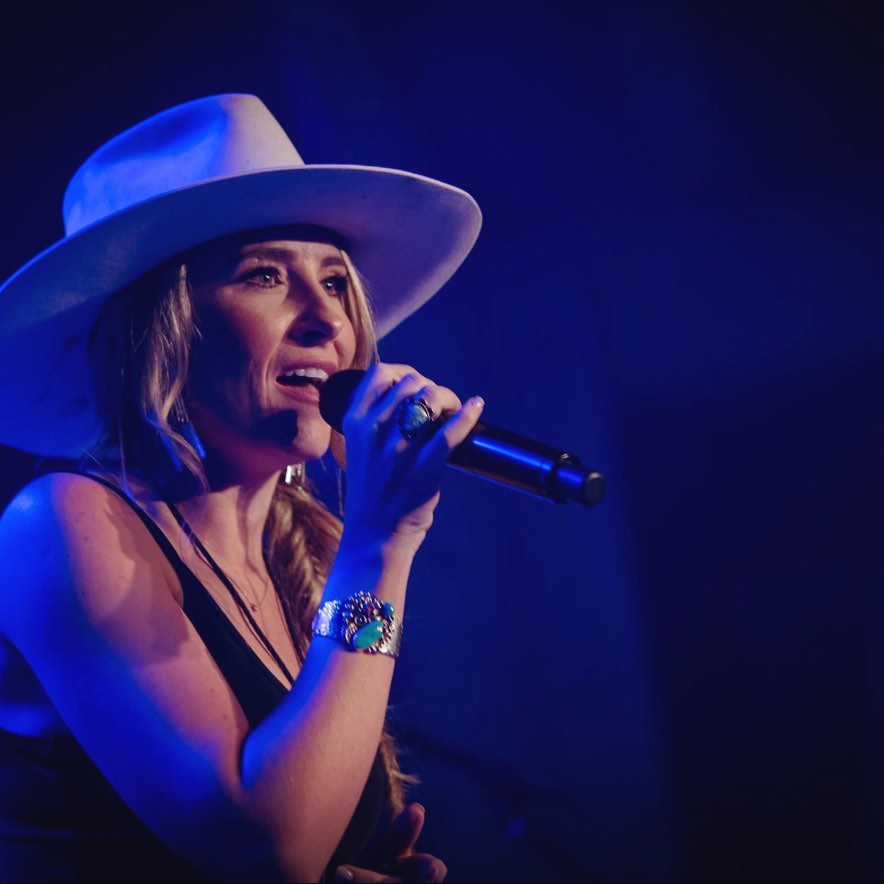 A woman singing on stage with blue lights in the background.