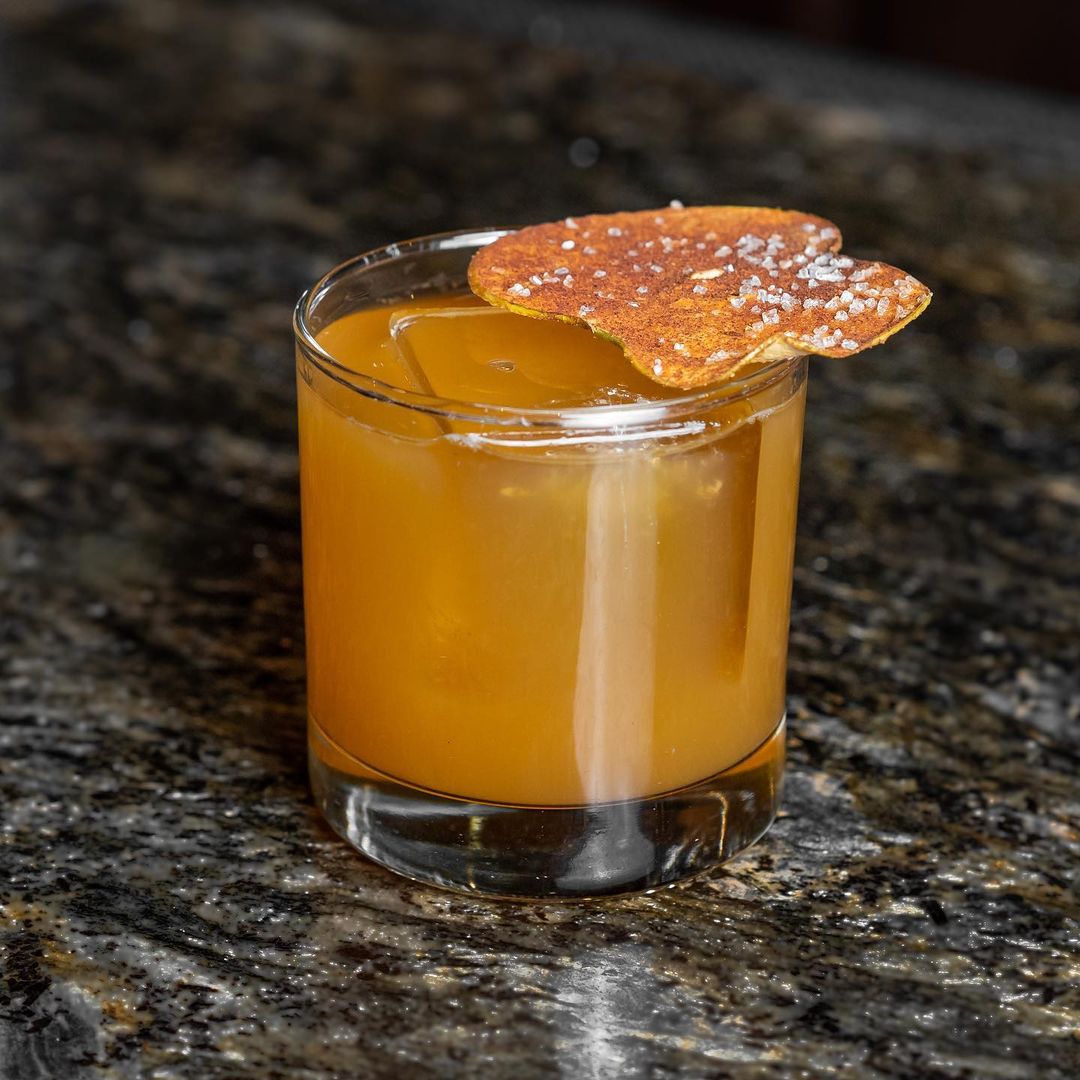 A rye whiskey cocktail with a citrus garnish on a bar top.