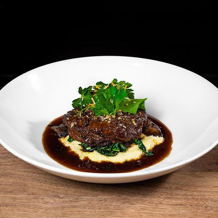 A dish with the Veal Osso Buco on top of creamy polenta.