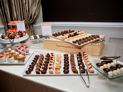 A table with trays of various small desserts and serving utensils.