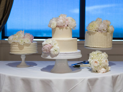 A table with 3 white cakes with flowers on top, next to bouquet of flowers and cake cutting utensils.