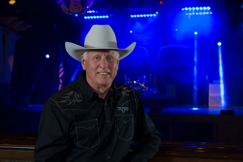 Andrew Edwards, in his white cowboy hat and black western shirt standing in front of the blue-lit stage.