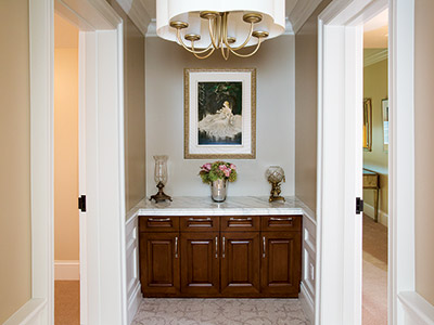 An entrance to The Suites with a chandelier, built in cabinets, flowers, andles, and doors to two private rooms.