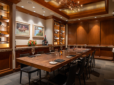 Elegant private dining space featuring a long table, built-in wine displays, wood paneling, and overhead chandelier