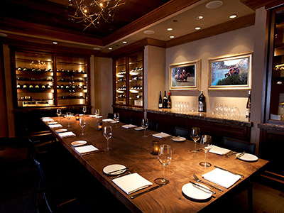 A room with a long dining table, chandelier, built-in wine cabinets, and a counter.