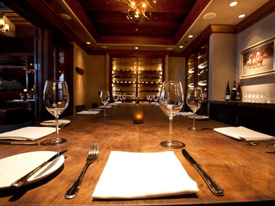 A close look of a long dining table, chandelier, built-in wine cabinets, and counter.