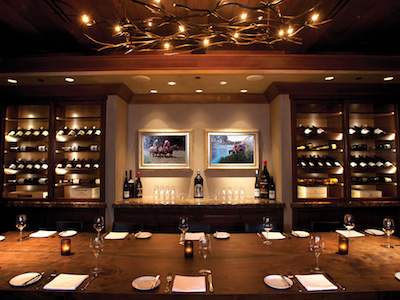 A room with a long dining table, chandelier, and built-in wine cabinets.