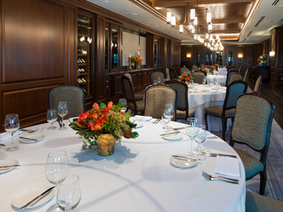 The Dining Room's wood floor, ceiling, panels, round tables set with flowers and flatware, built-in wine cabinets, and bar.