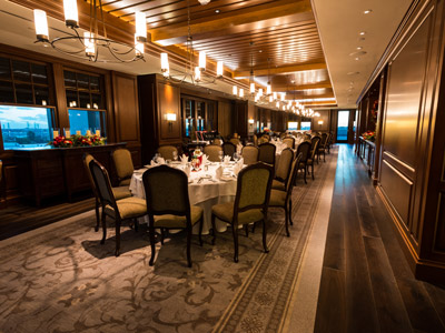 The Dining Room's wood floor, ceiling, panels, round tables set with flowers, Christmas decorations and flatware, and access to a terrace.