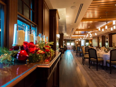 The Dining Room's wood floor, ceiling, panels, round tables set with flowers, Christmas decorations and flatware, and access to a terrace.