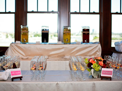 A buffet table set with wine glasses and flowers, in front of another buffet table set with different sangrias.