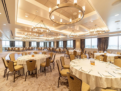 An elegant dining setup with round tables, gold-upholstered chairs, modern circular light fixtures, and expansive windows overlooking the surroundings.