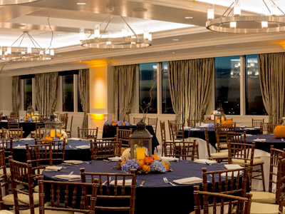 The Great Room set up set up with round tables with lantern and tiny pumpkin centerpieces.