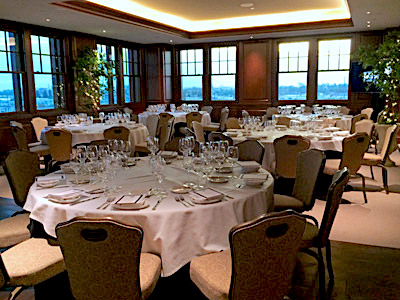 The Hospitality Suite set with dining tables, tan chairs, and a TV monitor.