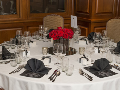 A round table with red flowers, candles, and tan chairs.