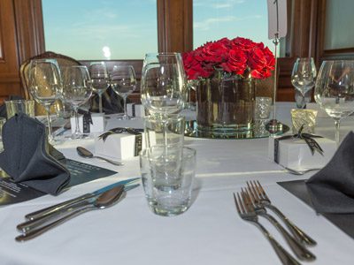 A round table with red flowers, and candles, next to a set of windows.