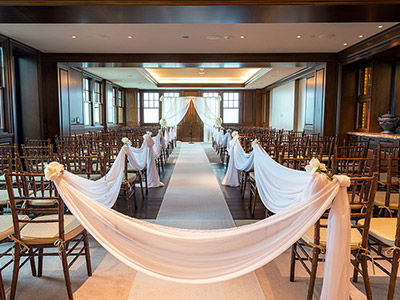 The Hospitality Suite arranged for a wedding ceremony, with two sections of chairs with a white carpet down the center aisle.