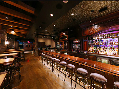 Inside the Ranch Saloon showing a bar, stools, wooden tables and chairs, and looking out towards the entrance.