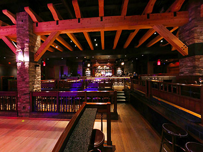 A view of the right side of the Ranch Saloon showing a wooden dance floor, tables and chairs, booth seating, and a bar.