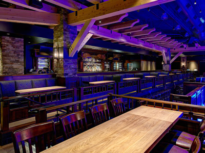 A wooden table with chairs, overlooking booth seating and a bar