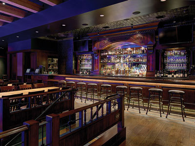 A bar with stools next to wooden tables and chairs and the entrance to a dance floor