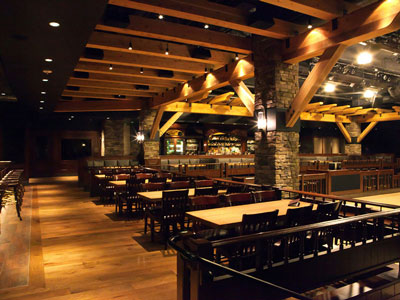 A row of wooden table and chairs next to a dance floor, looking at booth seating and a bar